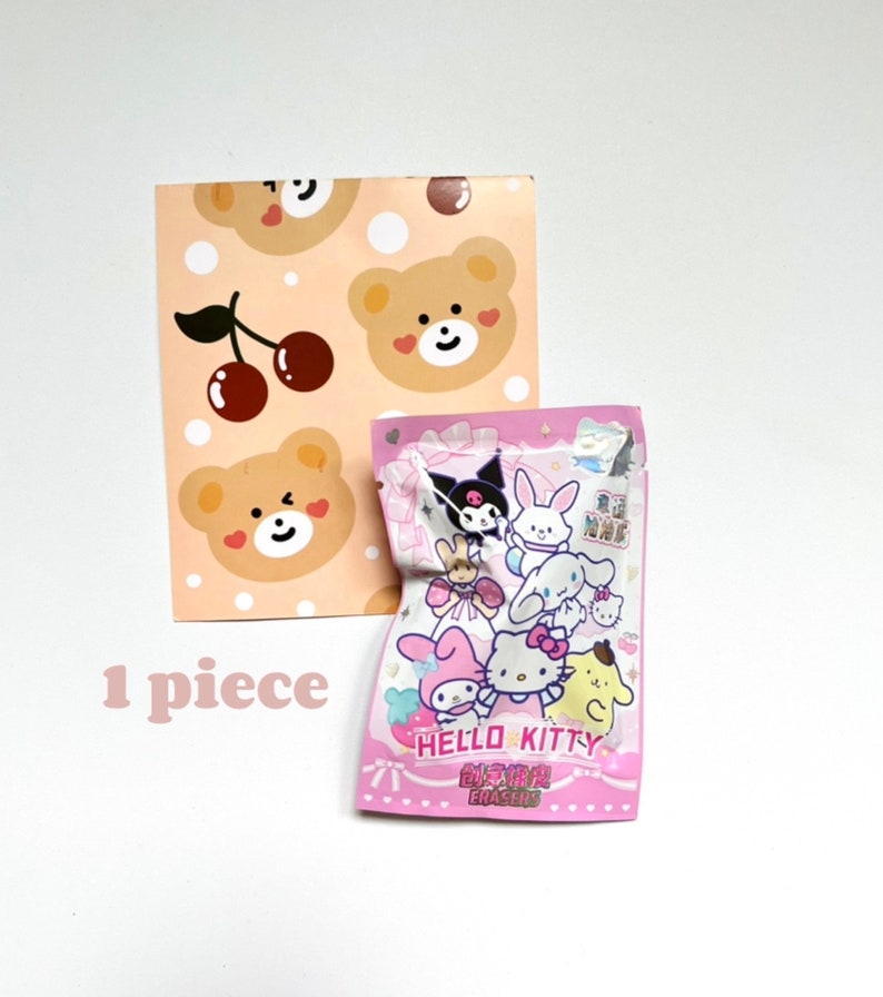 May include: A pink and white Hello Kitty eraser pack featuring a variety of Hello Kitty characters. The pack is on a white background with a pink and brown patterned paper behind it. The text on the pack reads "Hello Kitty Erasers".
