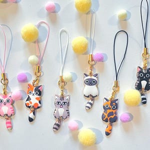 May include: Seven colorful cat charm phone straps with different colored cords. The charms are all different cat breeds with different expressions.