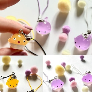 May include: A set of six colorful phone charms featuring a variety of designs, including pufferfish and whales. The charms are made of clear plastic and have a glossy finish. The charms are attached to colorful cords.