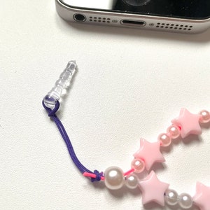 Op de afbeelding: Een roze en witte stervormige kralenbedel met een transparante plastic telefoonbedel bevestiging en een paars koord.