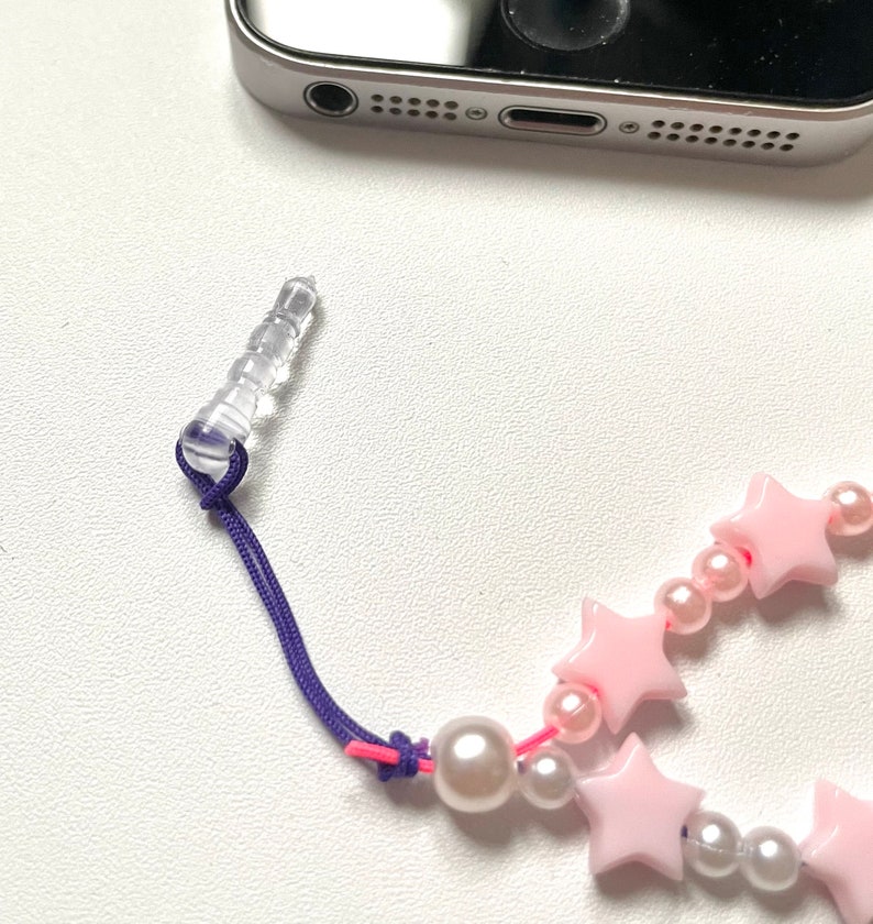 Op de afbeelding: Een roze en witte stervormige kralenbedel met een transparante plastic telefoonbedel bevestiging en een paars koord.
