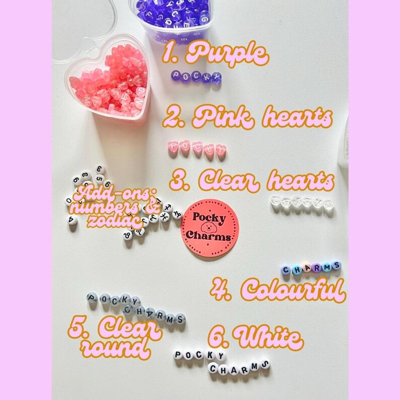 Op de afbeelding: Assortiment van kleurrijke kralen voor het maken van sieraden. Bevat paarse, roze en heldere hartvormige kralen, heldere ronde kralen en witte letterkralen die "Pocky Charms" spellen.