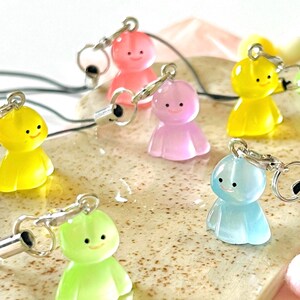May include: A set of six colorful, smiling, cartoon character keychains. The keychains are made of translucent plastic and come in yellow, pink, purple, light blue, and green.