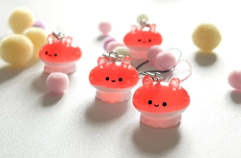 May include: Four pink and red jelly-like octopus charms with smiling faces. The charms are attached to silver chains and have a white base.