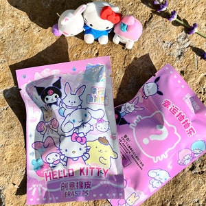 May include: Two pink plastic bags with Hello Kitty and other cartoon characters printed on them. The bags contain small eraser toys. The text on the bags reads "Hello Kitty Creative Erasers" and "Lucky Draw".