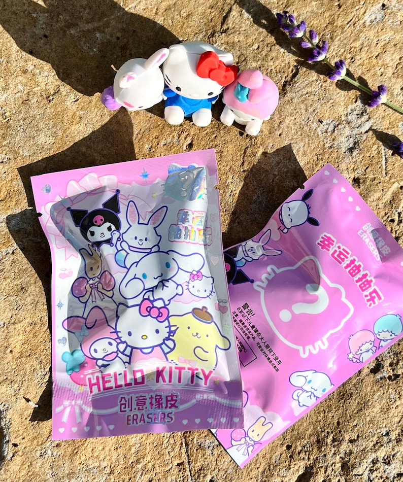 May include: Two pink plastic bags with Hello Kitty and other cartoon characters printed on them. The bags contain small eraser toys. The text on the bags reads "Hello Kitty Creative Erasers" and "Lucky Draw".