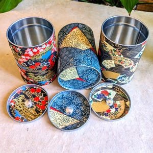 Peut inclure: Trois récipients cylindriques en métal avec couvercles, décorés de papier de style japonais. Les récipients présentent des motifs floraux, de vagues et d'éventails en rouge, or et bleu. Les couvercles ont des boutons argentés.
