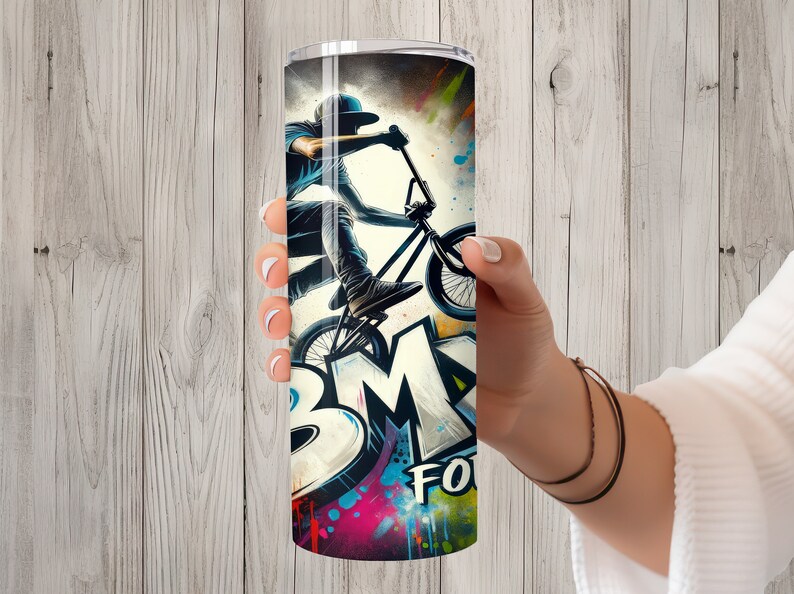 May include: A stainless steel tumbler with a colorful graphic of a person riding a BMX bike. The graphic includes the word "BMX" in large, stylized letters. The background is a mix of colorful paint splatters.