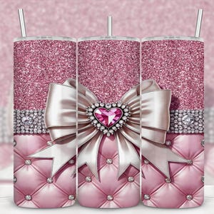 May include: A pink glitter tumbler with a white bow and a heart-shaped jewel. The tumbler features a diamond-like band and a quilted pattern at the base. It includes a silver straw.