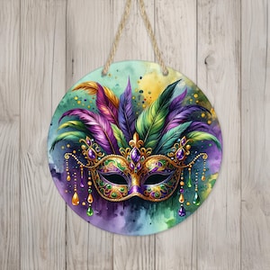 May include: A round wooden sign with a colorful Mardi Gras mask and feathers. The mask is gold, purple, and green with jewels. The background is a watercolor wash of purple, green, and blue.