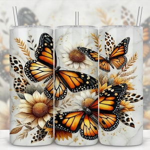 May include: A set of three stainless steel tumblers with a butterfly and floral design. The design features orange and black monarch butterflies, sunflowers, and leopard print accents against a marble background. Each tumbler has a silver straw.