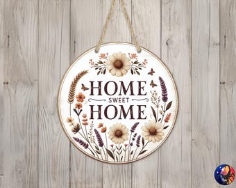 Könnte beinhalten: Ein rundes Holzschild mit weißem Hintergrund und einem floralen Design. Das Schild trägt die Aufschrift "Home Sweet Home" in braunen Buchstaben.