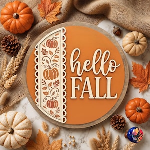 May include: A circular wooden sign with a smooth orange background featuring the text "hello FALL" in white lettering. To the left, a vertical decorative panel displays a cream-colored cutout pattern of pumpkins and leaves on a brown base.