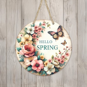 May include: Round wooden sign featuring a floral wreath and butterflies. The sign reads "Hello Spring" in teal lettering.