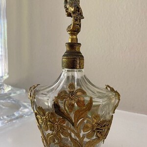 May include: A vintage glass perfume bottle with a gold-toned metal floral design and a cherub-shaped stopper.