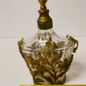 May include: A vintage glass perfume bottle with a gold-toned stopper and intricate floral design. The bottle is approximately 3 inches tall.