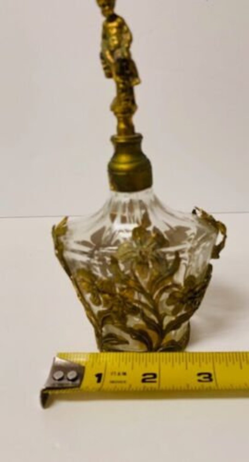 May include: A vintage glass perfume bottle with a gold-toned stopper and intricate floral design. The bottle is approximately 3 inches tall.