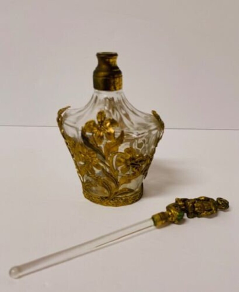 May include: A vintage glass perfume bottle with a gold floral design and a matching glass and gold dropper.