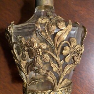 May include: A vintage glass perfume bottle with a gold floral design. The bottle is clear and has a textured surface.