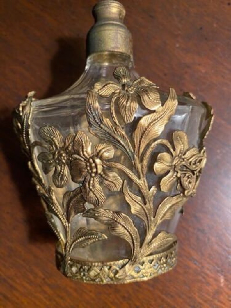 May include: A vintage glass perfume bottle with a gold floral design. The bottle is clear and has a textured surface.