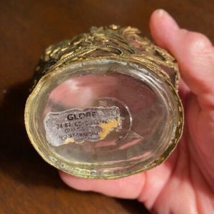 May include: A gold-colored glass bottle with a decorative lid and a label that reads "GLOBE 24 KT GOLD PLATE  MADE IN JAPAN  NORTHERN SUPPLY".