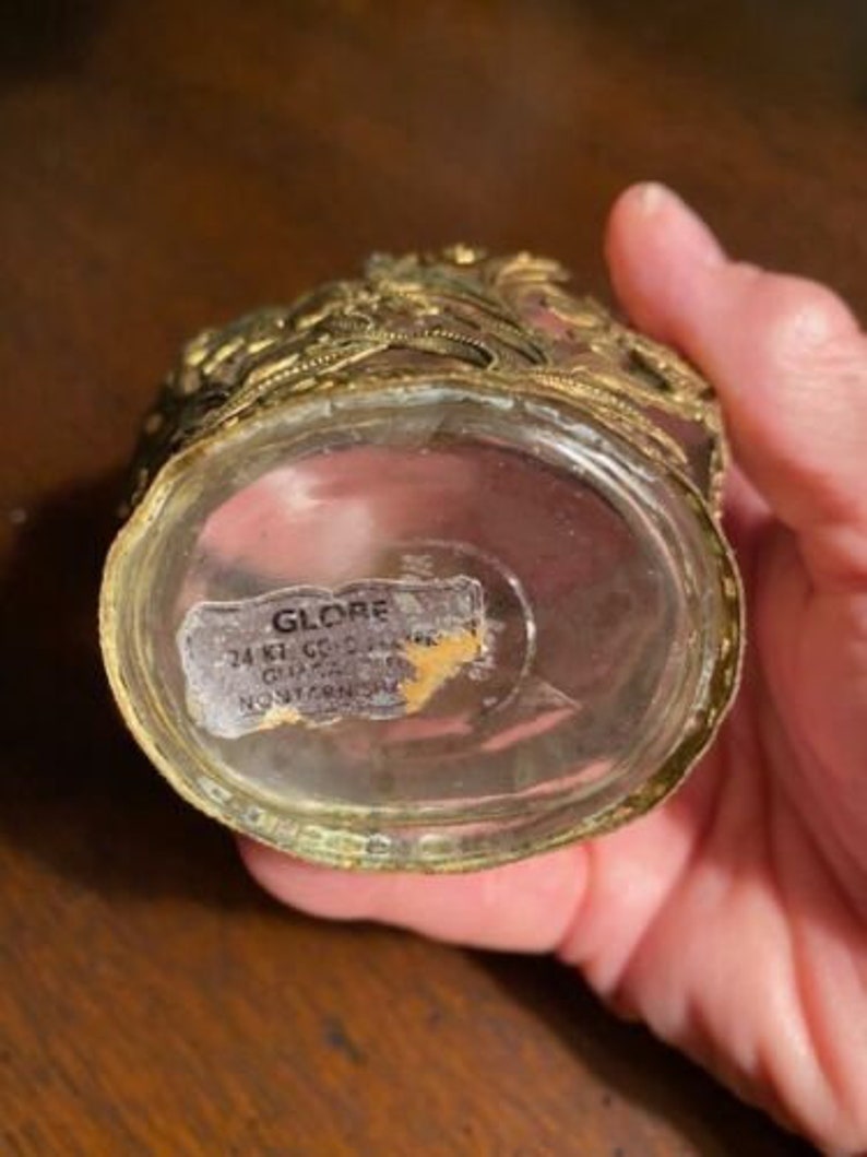 May include: A gold-colored glass bottle with a decorative lid and a label that reads "GLOBE 24 KT GOLD PLATE  MADE IN JAPAN  NORTHERN SUPPLY".