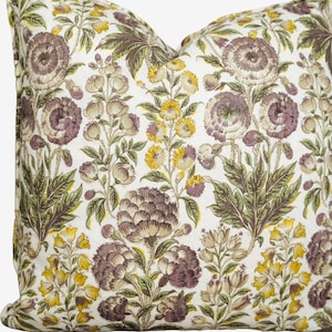 May include: Square decorative pillow with a floral pattern. The pillow features a white background with a repeating design of purple, yellow, and green flowers and leaves. The pillow is a square shape.