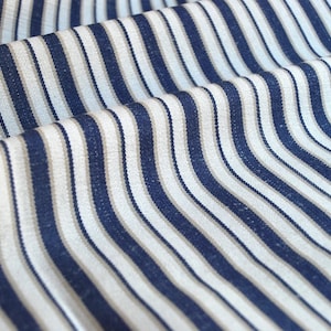 May include: A close-up of a striped fabric with alternating white and navy blue stripes. The fabric is woven with a textured, slightly rough surface.