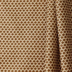 May include: Close-up of a fabric with a repeating pattern of small, brown floral shapes on a cream-colored background. The fabric is draped, showing folds and texture. The overall effect is a classic, decorative textile.