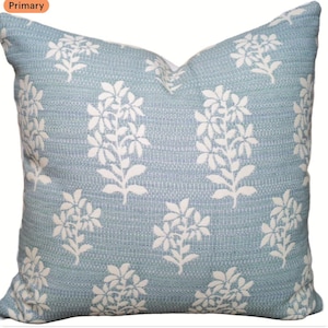 May include: A square decorative pillow with a light blue background and a repeating white floral pattern. The pillow has a textured appearance and is designed for home decor.
