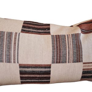 May include: Rectangular decorative pillow with a patchwork design. The pillow features squares and stripes in cream, brown, and gray tones. The pillow is a home decor item.