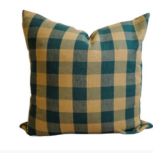 Könnte beinhalten: Quadratisches Zierkissen mit einem teal- und beigefarbenen Karomuster. Das Kissen hat ein weiches, strukturiertes Aussehen und einen klassischen Landhausstil. Das Kissen hat eine quadratische Form und eignet sich für ein Sofa oder Bett.