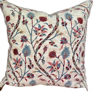 May include: Square decorative pillow with a cream-colored background and a floral pattern in shades of red, blue, and beige. The design features stylized flowers and branches.