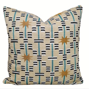 May include: Square cushion with a beige background featuring a geometric design. The pattern incorporates black, white, and teal lines, alongside gold star shapes. The cushion has a soft, textured appearance and would suit a living room.