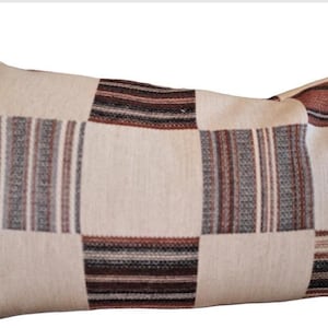 Może przedstawiać: Prostokątna poduszka dekoracyjna z patchworkowym wzorem. Poduszka ma kwadraty i prostokąty w odcieniach kremu, brązu i szarości. Wzór zawiera zarówno jednolite, jak i paskowane wzory, tworząc teksturowany wygląd.