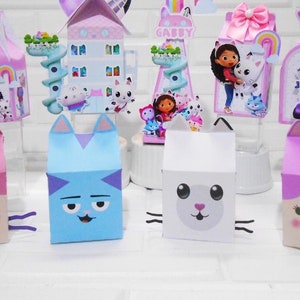 May include: A set of colorful party favor boxes featuring characters from the children's show Gabby's Dollhouse. The boxes are shaped like cats and feature different characters from the show, including Gabby, Pandy Paws, and Cakey. The boxes are perfect for holding small treats or toys for a Gabby's Dollhouse themed party.