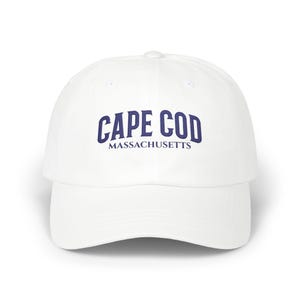 Puede incluir: Gorra de béisbol blanca con las palabras "CAPE COD" en azul marino, arqueadas en la parte delantera, con "MASSACHUSETTS" debajo. La gorra tiene una visera curva y una corona redonda.