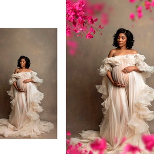 May include: A pregnant woman in a white, flowing gown with ruffles stands in front of a brown backdrop. Pink flowers are blurred in the background.