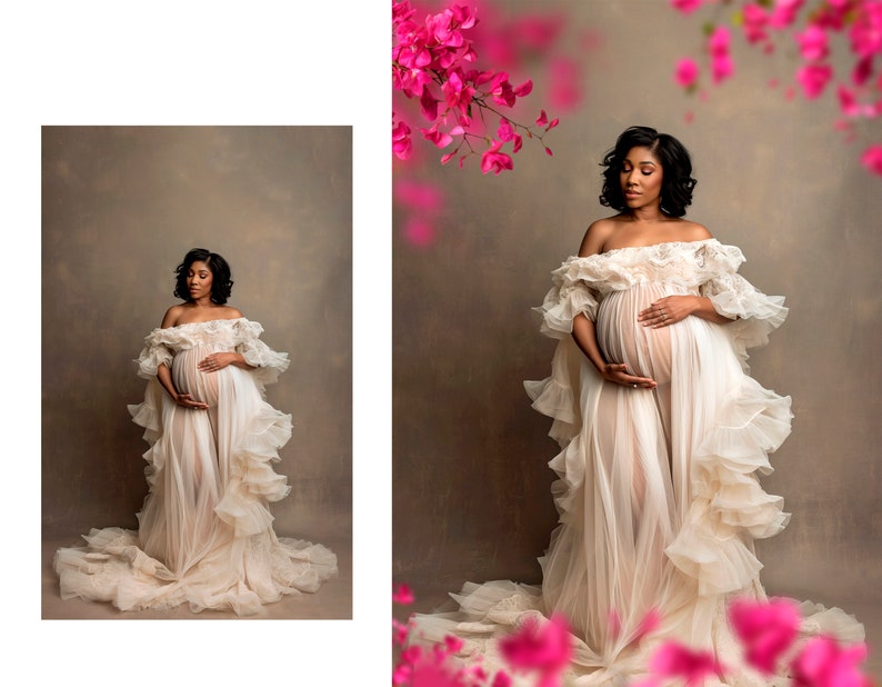 May include: A pregnant woman in a white, flowing gown with ruffles stands in front of a brown backdrop. Pink flowers are blurred in the background.