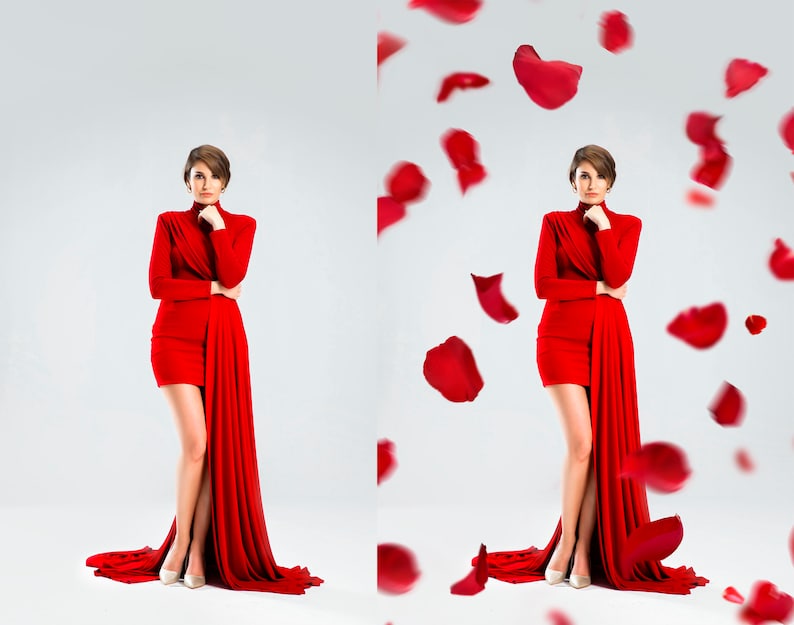 May include: A woman in a red dress with a long train stands in front of a white background.  She is looking to the side and has her hand on her chin.  Rose petals are falling around her.