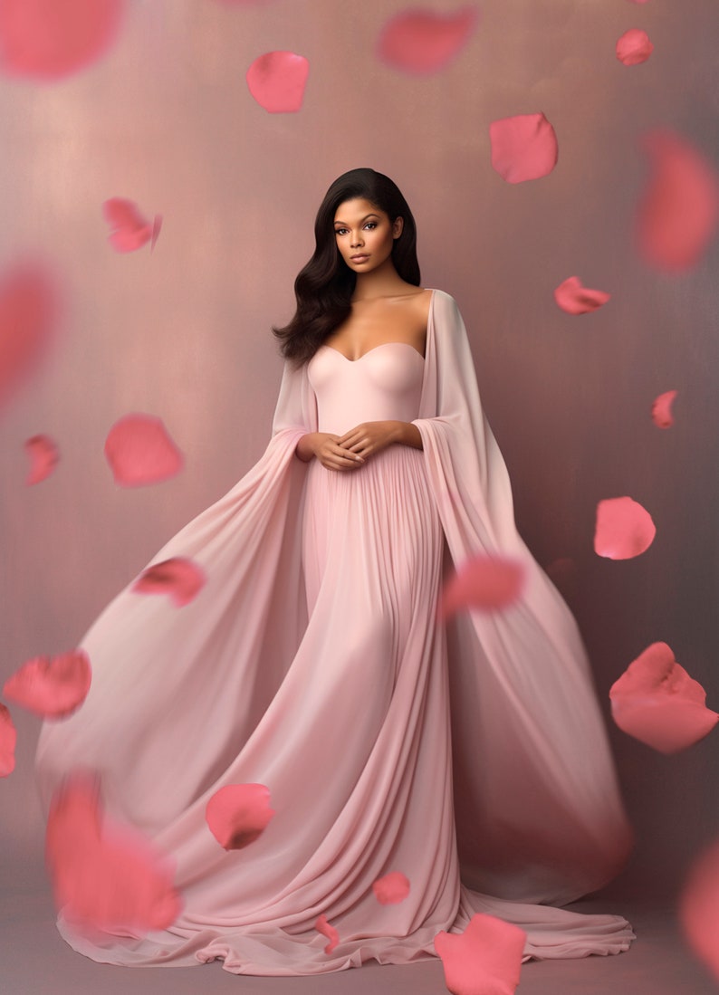 May include: A strapless, pale pink gown with a flowing cape. The dress features a pleated skirt and is worn by a person with dark hair. Pink rose petals float in the air, creating a soft, romantic atmosphere.
