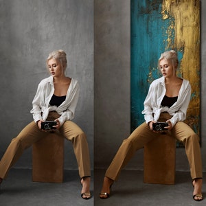 May include: A woman wearing a white shirt and brown pants sits on a stool in front of a blue and gold abstract painting. She is holding a vintage camera in her hands.