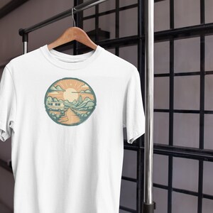 May include: White t-shirt featuring a circular graphic of a camper van driving through a mountain landscape with a sun and clouds in the background.