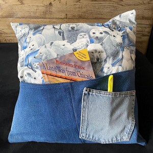 May include: A blue denim pillow with a pocket on the front. The pocket has a yellow highlighter and a book titled "A Long Way from Chicago" by Richard Peck. The pillow is decorated with a white fabric featuring a pattern of polar bears and other arctic animals.