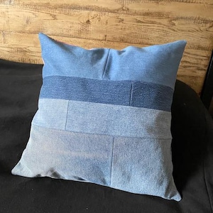 May include: A blue denim pillow with a patchwork design. The pillow is made from different shades of blue denim and has a simple, rectangular shape.