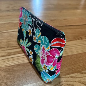 May include: A black zippered pouch with a tropical floral print featuring pink, green, yellow, and white flowers on a black background.