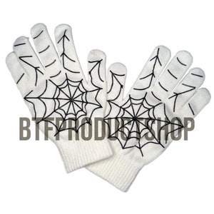 May include: A pair of white knit gloves with a black spiderweb design. The gloves are shown with the palms facing out.