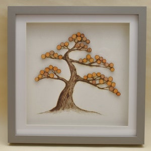 May include: A framed artwork featuring a stylised tree made of small wooden circles, painted in shades of orange and brown, on a white background.