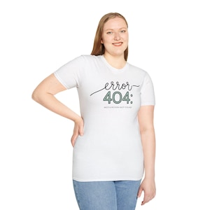 May include: A white short-sleeved t-shirt featuring the black cursive text error, the green numerical text 404:, and the smaller black text MOTIVATION NOT FOUND printed on the chest. The shirt has a crew neckline and a standard fit.