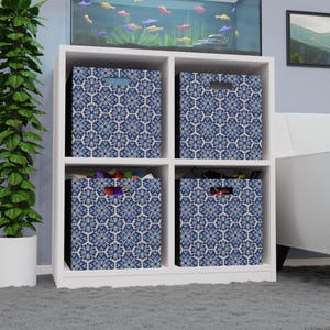 Könnte beinhalten: Ein weißes Würfelregal mit vier Stoff-Aufbewahrungsboxen. Jede Box hat ein blau-weißes Blumenmuster. Die Boxen sind mit verschiedenen Gegenständen gefüllt, was auf eine Aufbewahrungslösung für die Organisation zu Hause hindeutet.